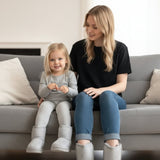 Woman and child wearing sparkly gray winter boots sitting on a gray couch in a living room setting.
