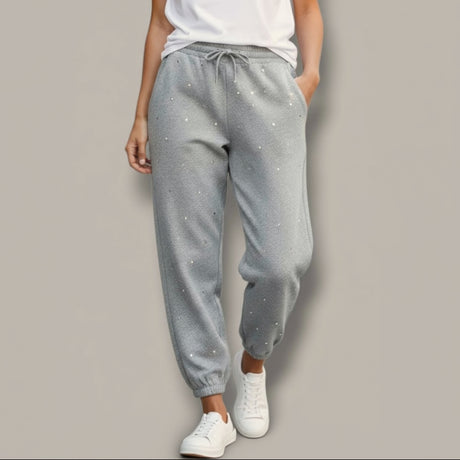 Person wearing gray sparkly sweatpants with small embellishments on a plain background