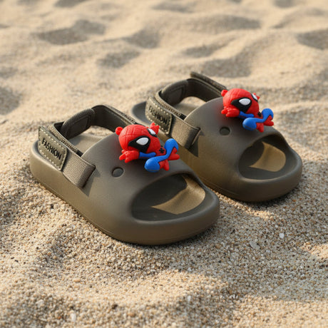 Pair of khaki green kids slides with heel straps and 3D Spiderman charms on sand