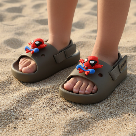 Kids olive green slides with red Spiderman charms, worn barefoot on soft beach sand
