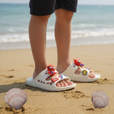 White double strap slides with Spiderman head charms worn by a child on warm sand