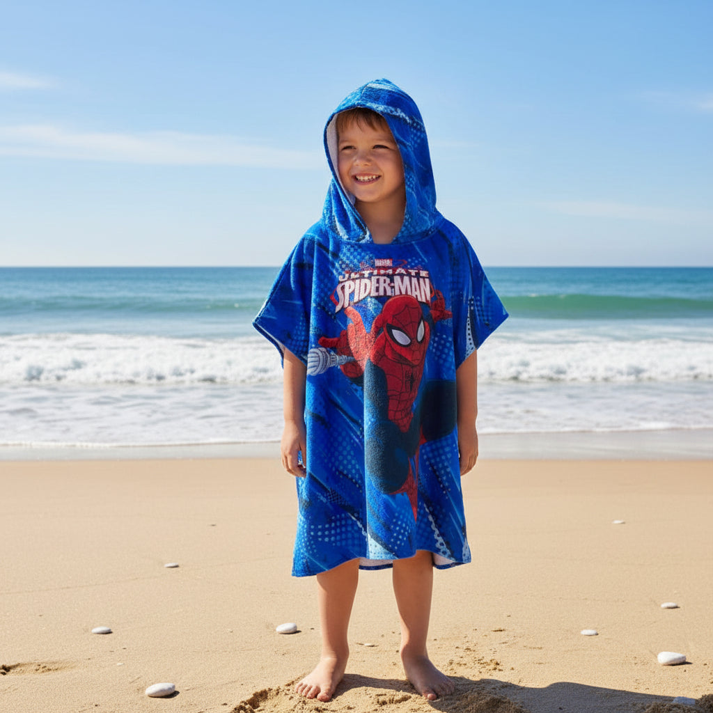 Boy wearing a cobalt blue Spiderman hooded poncho towel on the beach