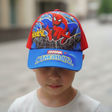 Boy in a white top wearing a red and blue kids cap printed with a swinging superhero character