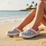 Grey and pink foam beach clogs with ventilation holes worn on sand
