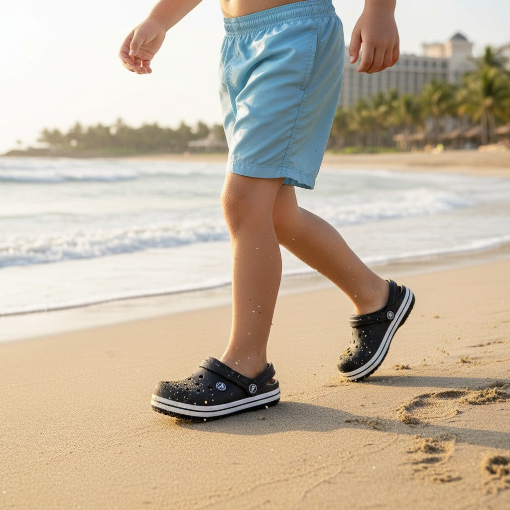 Child walking along wet sand in black foam clogs with a white midsole stripe