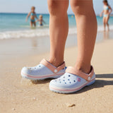 Pale blue foam clogs with peach back straps standing on damp shoreline sand