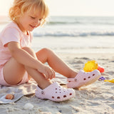Child in a pink tee sitting on a beach towel wearing pale pink foam clogs