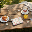 Spotted tapestry crossbody bag with a gold chain on a garden table