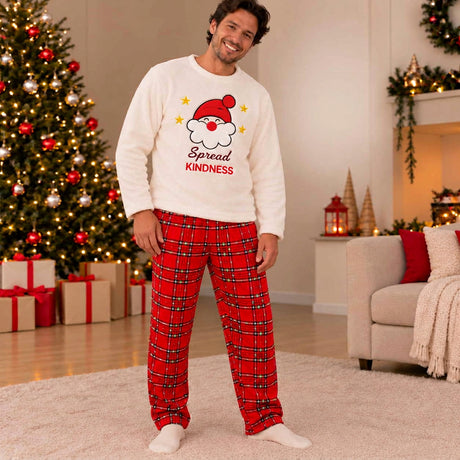 Man in cream Spread Kindness Santa fleece top and red plaid pyjama pants in a festive living room