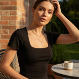 Woman wearing a black square neck top at an outdoor cafe table