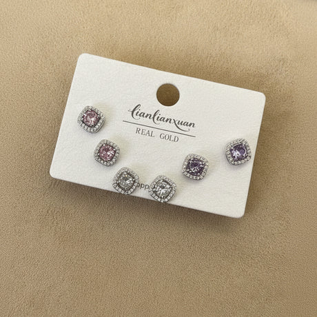 Set of square stud earrings on a display card on a beige surface