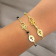 Gold bracelet with black beads and St Charbel symbol on a wrist against a neutral background