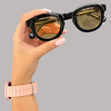 Hand holding a pair of black stargaze sunglasses with gold reflective lenses against a grey background