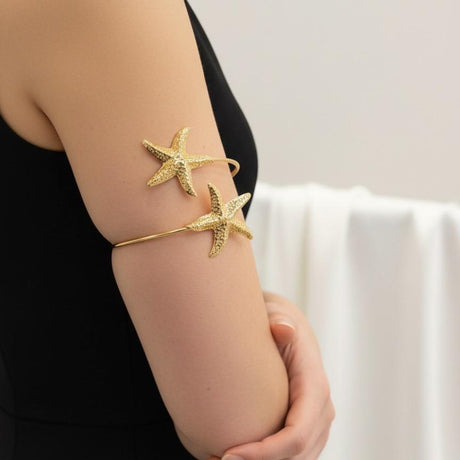 Gold star cuff bracelets on a person's wrist against a neutral background