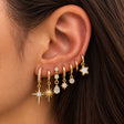 Ear stacked with gold star earrings including a crystal north star, starburst and white enamel star
