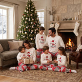 Family of six in matching cream snowman tops and Fair Isle pyjama pants by a fireplace and tree
