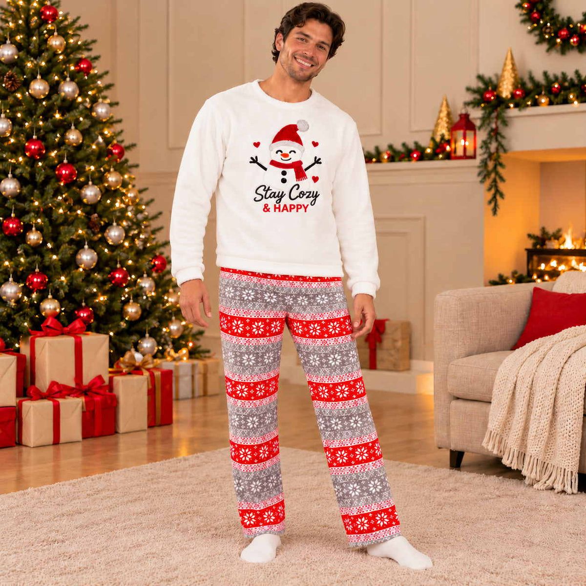 Man in cream Stay Cozy snowman fleece top and red and grey snowflake pyjama pants in a festive room