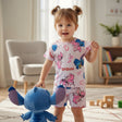 Child wearing a 'Lilo & Stitch' themed outfit holding a plush toy in a room with a chair and books