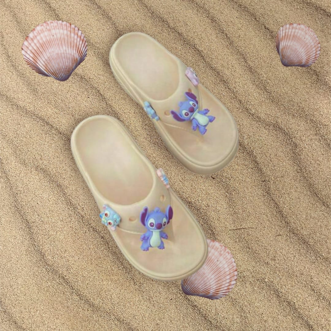Top down view of sandy beige flip flops with blue Stitch charms on rippled sand