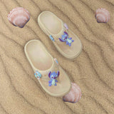 Top down view of sandy beige flip flops with blue Stitch charms on rippled sand