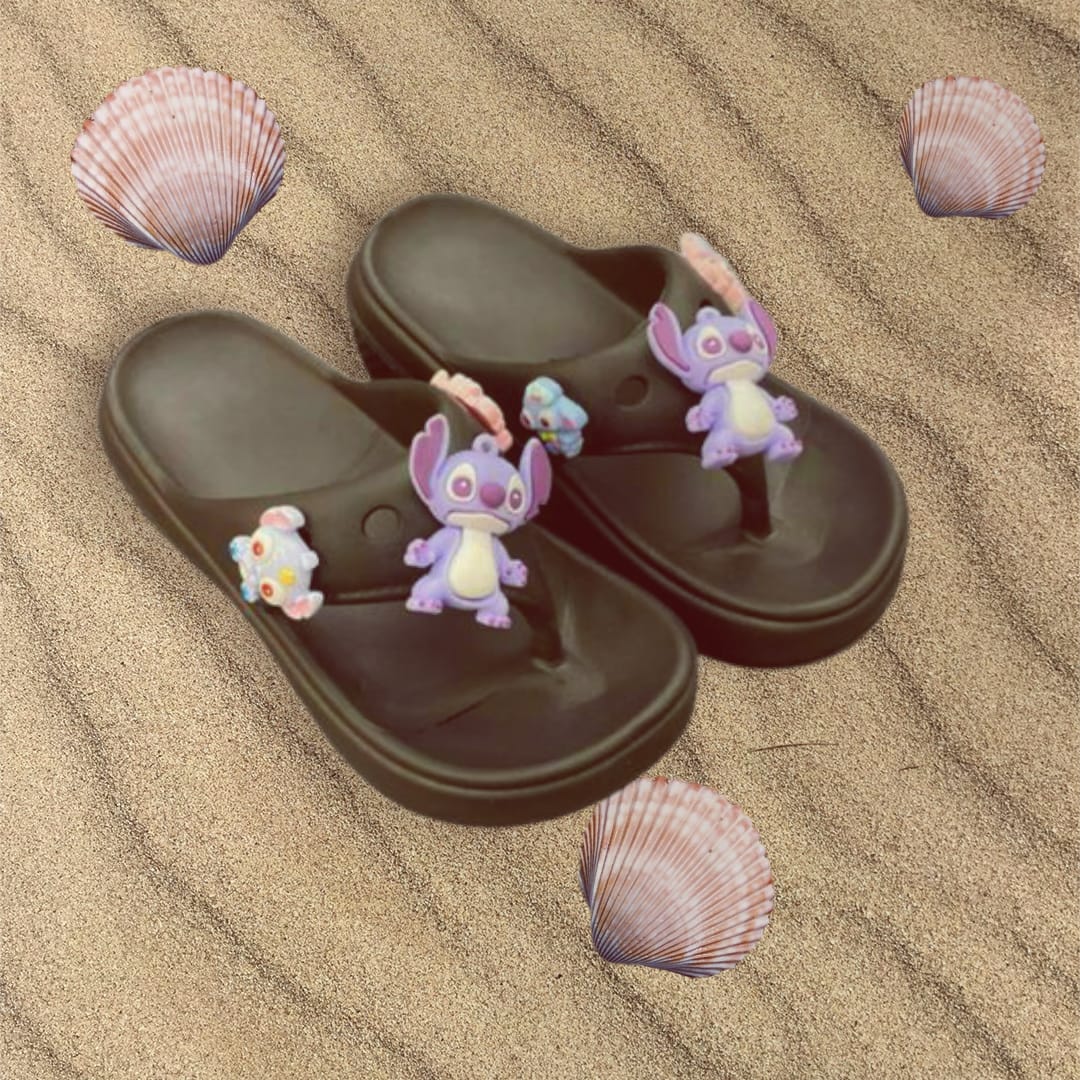 Dark brown thong sandals topped with purple and pink character charms on rippled sand