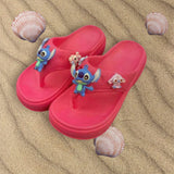 Pink cushioned flip flops with blue and pastel charms laid on rippled sand with shells
