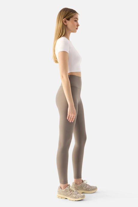 Woman wearing beige leggings and a white top on a white background