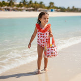 Girl in a strawberry and heart print onepiece swimsuit walking toward the camera on the beach