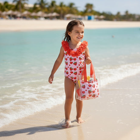 Girl in a strawberry and heart print onepiece swimsuit walking toward the camera on the beach