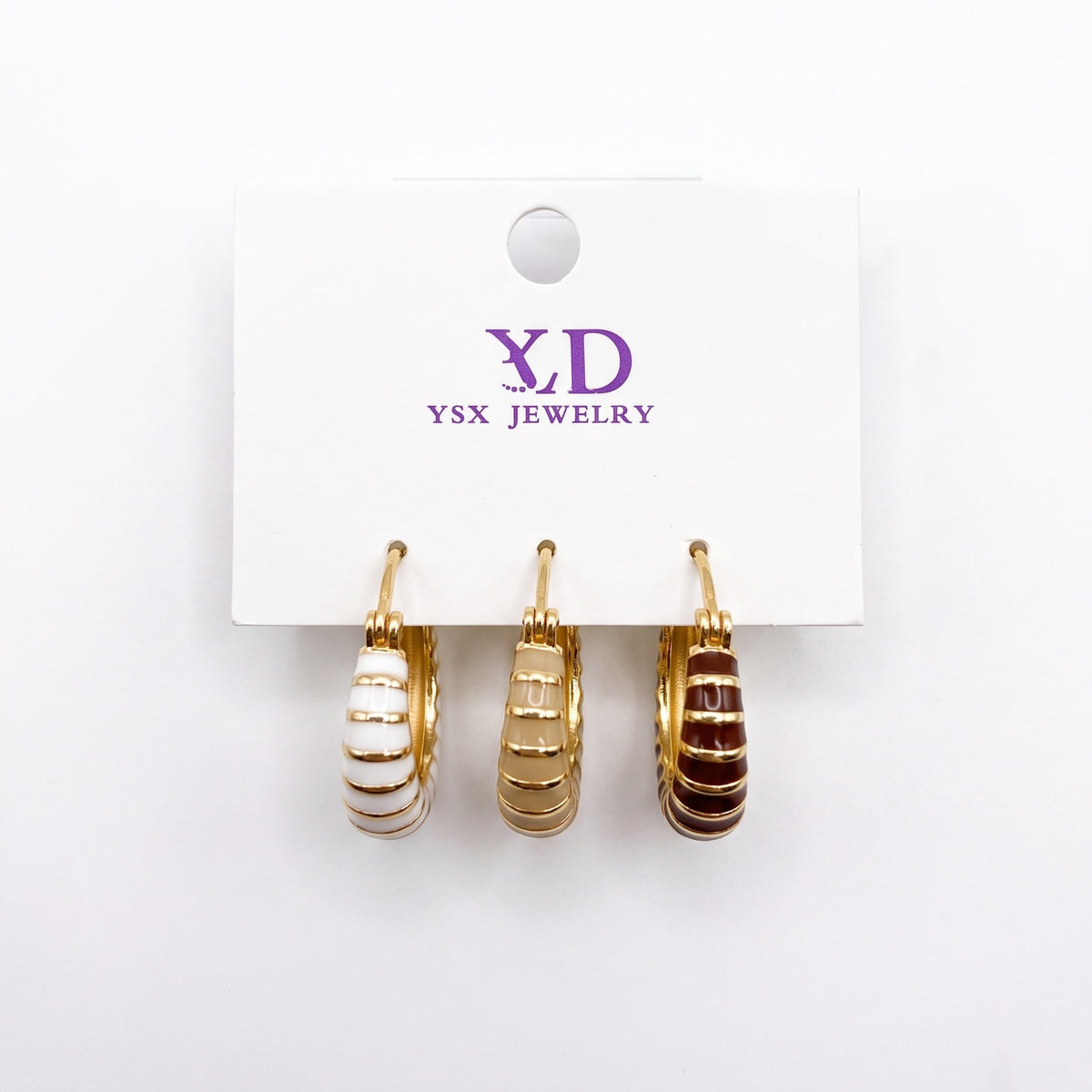 Three single striped enamel huggie earrings in white, beige and brown on a card