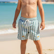 Young boy in striped swim shorts standing with small fish on a sandy beach