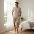 Man wearing a beige striped henley pyjama set in a bright bedroom