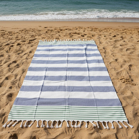 Striped tassel beach towel on sandy beach with ocean waves in background