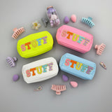 Four colorful 'STUFF' pouches in yellow, pink, blue, and white with accessories on a grey background