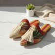 Colorful handmade slippers with tassels on a light surface with a plant and towel in the background