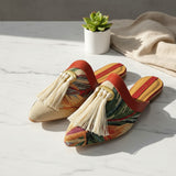 Colorful handmade slippers with tassels on a light surface with a plant and towel in the background