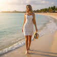 A woman walks along the shoreline wearing a fitted white sleeveless dress with a geometric knit pattern