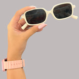 Hand holding a pair of white sun chic sunglasses with a grey background