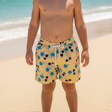 Child wearing yellow swim shorts with blue palm trees and sunglasses on a beach