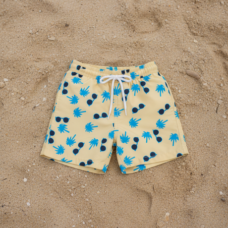 Beige shorts with blue palm trees and sunglasses on a sandy background
