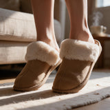 Woman standing on tiptoe in tan suede look slippers with cream fur collars in a sunny room