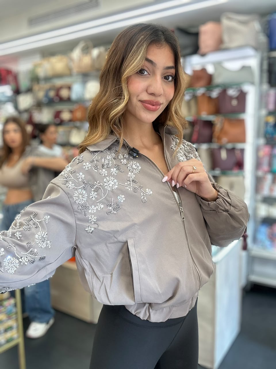 Taupe beaded floral bomber with puff sleeves and an elastic hem worn over black leggings in a shop