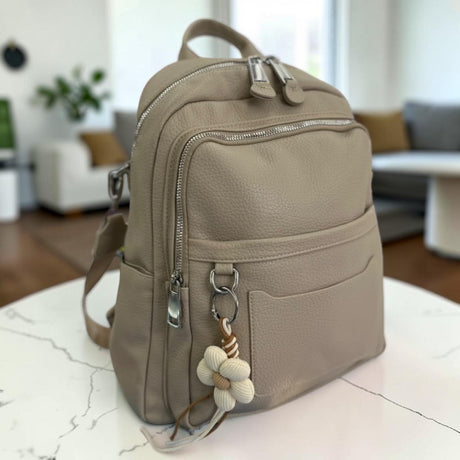 Taupe backpack on a round marble table, angled to show the side pocket