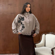 Woman in a taupe oversized jacket with black sequin flowers, a high collar and a brown satin skirt