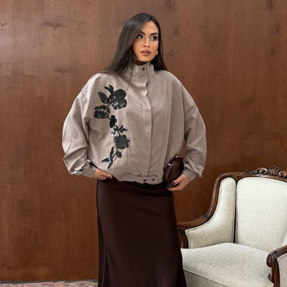 Woman in a taupe oversized jacket with black sequin flowers, a high collar and a brown satin skirt