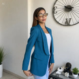 Side view of a teal blazer with a shawl lapel and flap pockets worn over a white top