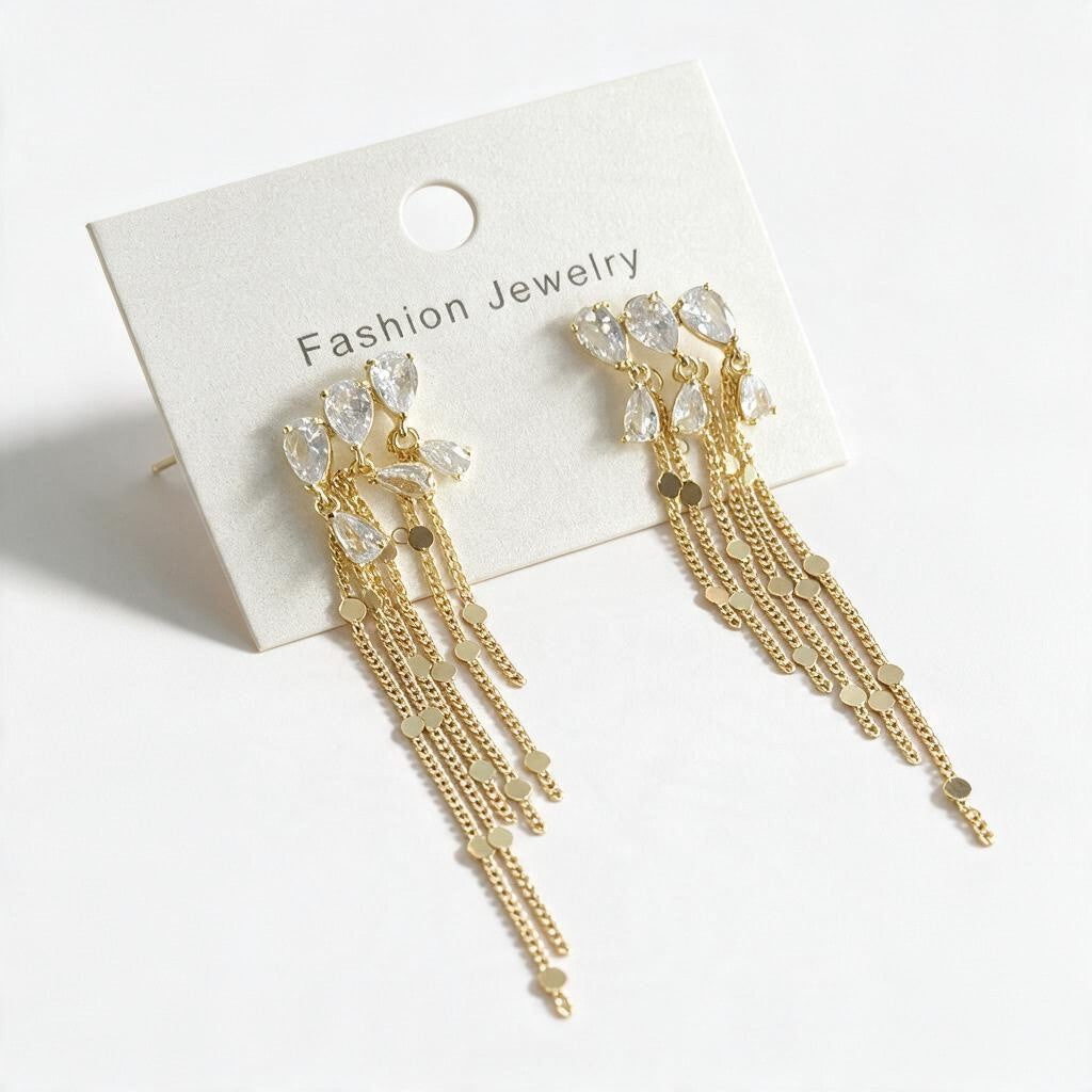 Gold teardrop crystal earrings with long fine chain tassels on a white card