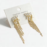 Gold teardrop crystal earrings with long fine chain tassels on a white card