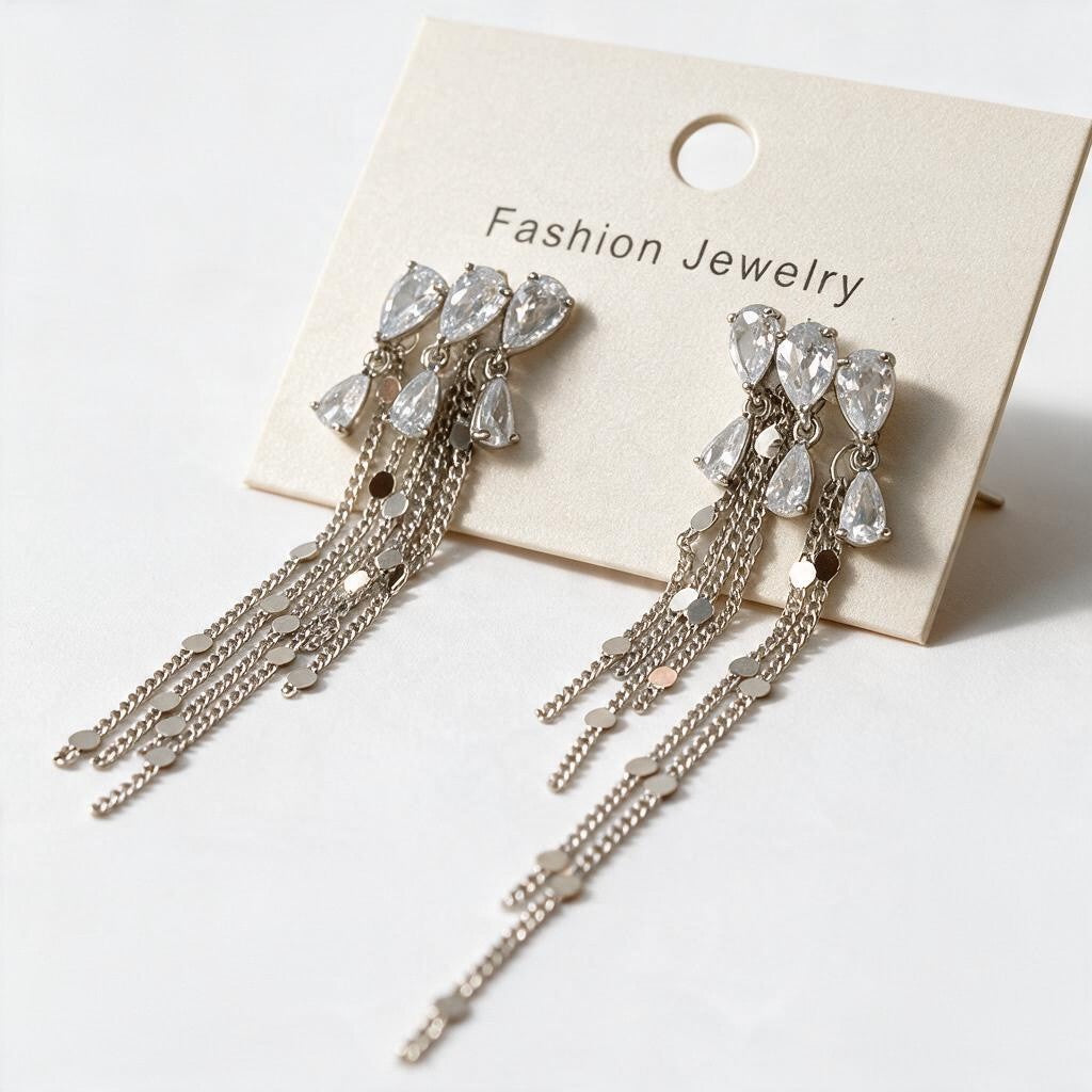 Pair of silver tone teardrop crystal tassel earrings on a cream display card