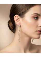 Close-up of a woman wearing gold teardrop earrings with clear stones on a beige background